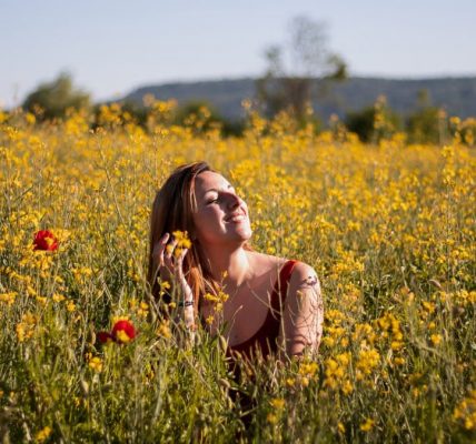 A woman sits with eyes closed, enjoying the sun in a vibrant yellow flower field.