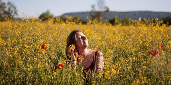 A woman sits with eyes closed, enjoying the sun in a vibrant yellow flower field.