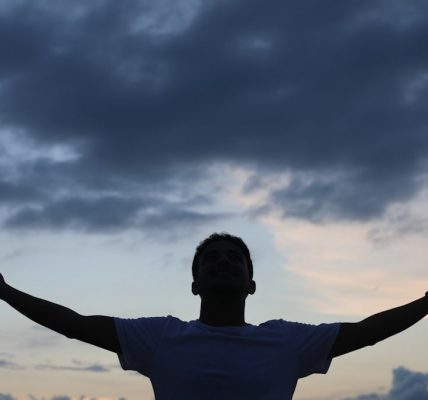 man in white t-shirt raising his hands under cloudy sky during daytime