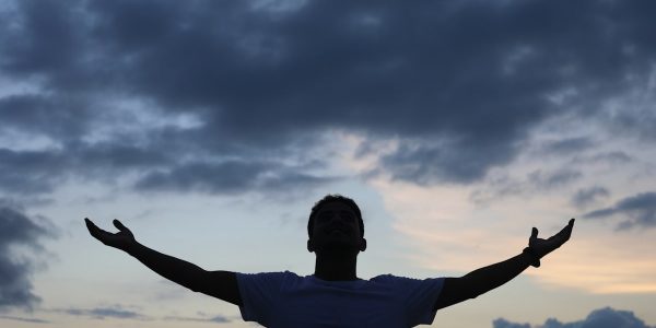 man in white t-shirt raising his hands under cloudy sky during daytime